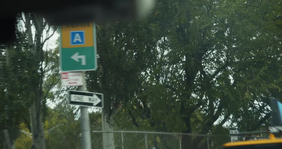 A view of traveling in a car on a neighborhood street behind a taxi with a busy highway seen beyond a fence on an overcast day