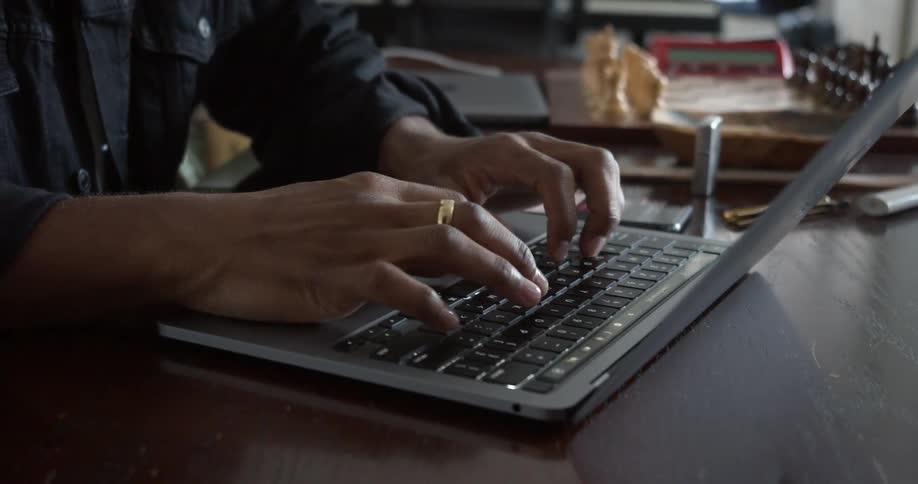 Man sits at desk near chess set typing on computer