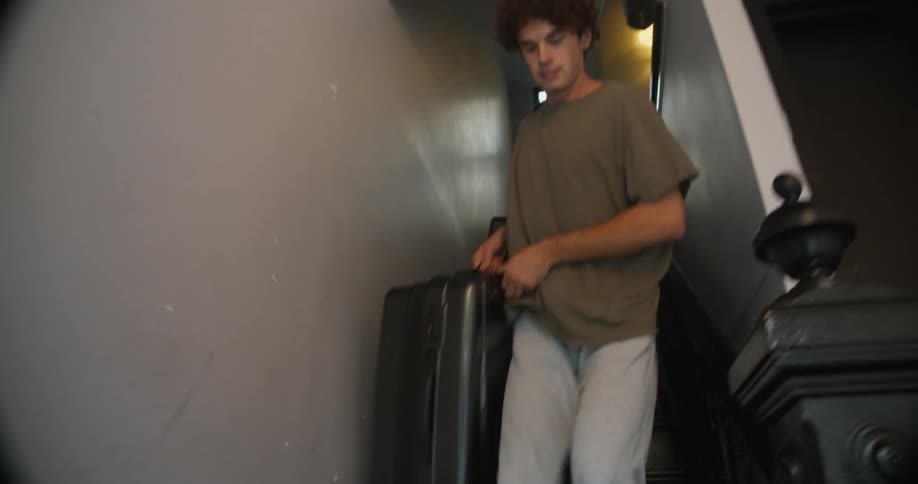 Man and woman carry luggage down staircase en route to door