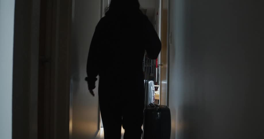 Man and woman roll luggage down corridor in wood floored home