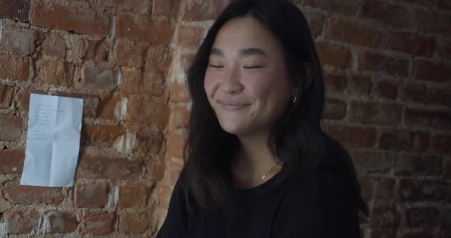 Young happy woman folding clothes to pack luggage in front of a red brick wall
