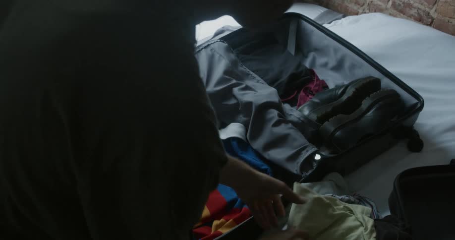 A woman packs clothes into a suitcase that is sitting on a bed
