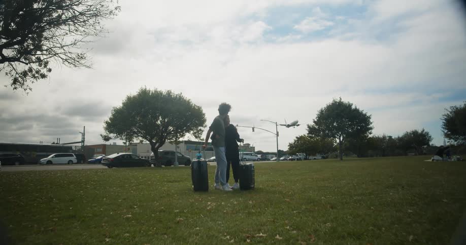 Couple stands on lawn near airport pointing at landing airplane