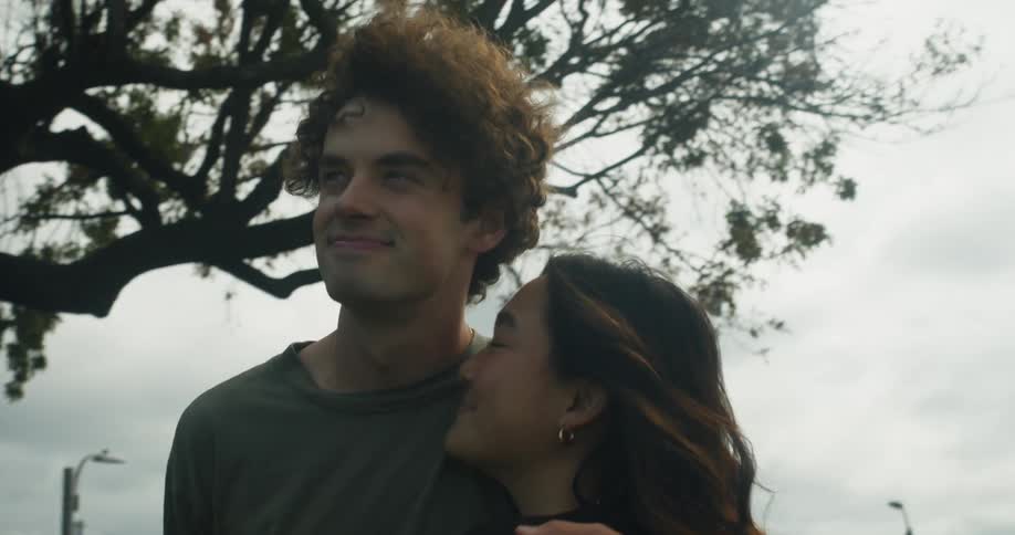 Man with curly hair and woman with straight hair hold each other and watch plane landing