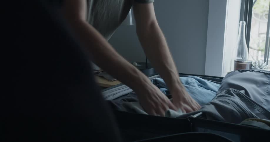 Man folds and packs suitcase as another person stands nearby