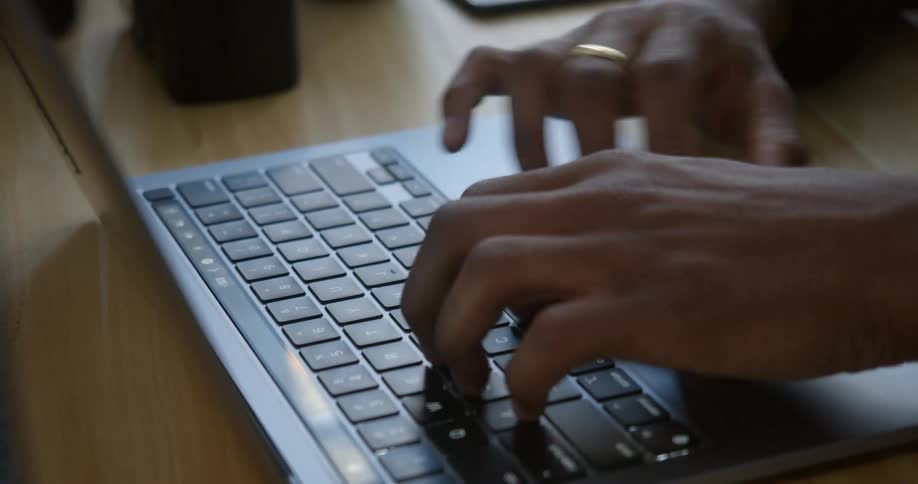 A man types on his laptop while sitting at a desk