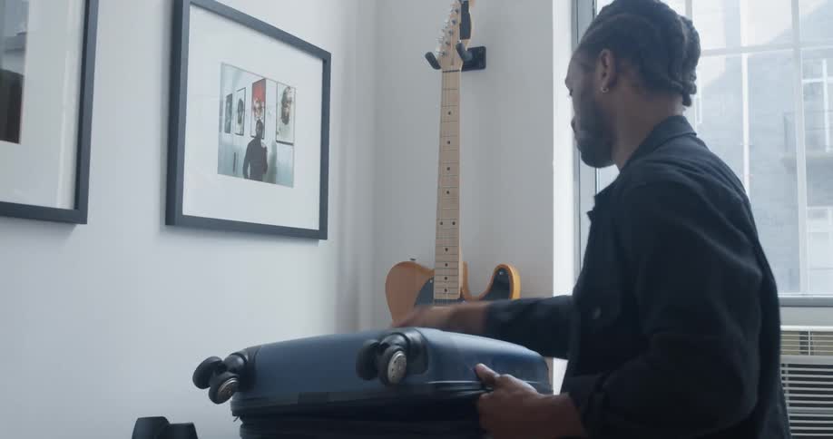 A man folds and packs clothing into a suitcase then closes it and places it on the bed