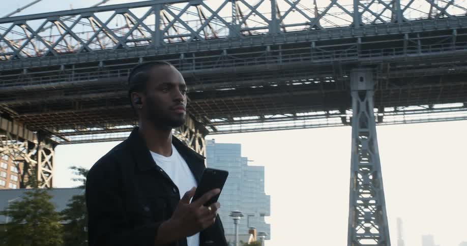 Man talks while holding mobile phone as he walks near base of bridge