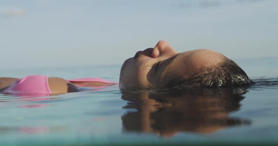 Young woman wearing a pink bikini floating in the ocean with eyes closed