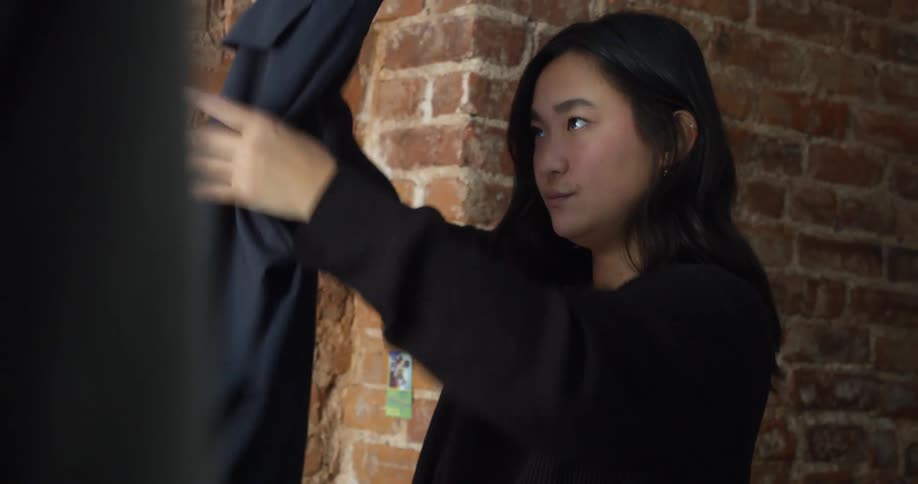 A woman is folding clothes indoors during the daytime while a man watches