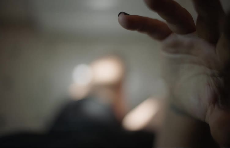 A woman sitting in a residential bathroom during the daytime raises her hand toward the camera