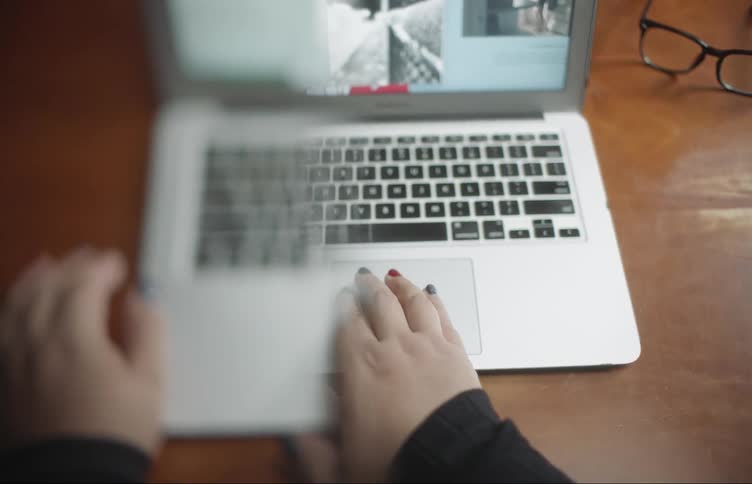 A woman opens a laptop and uses it without her glasses on causing half to blur