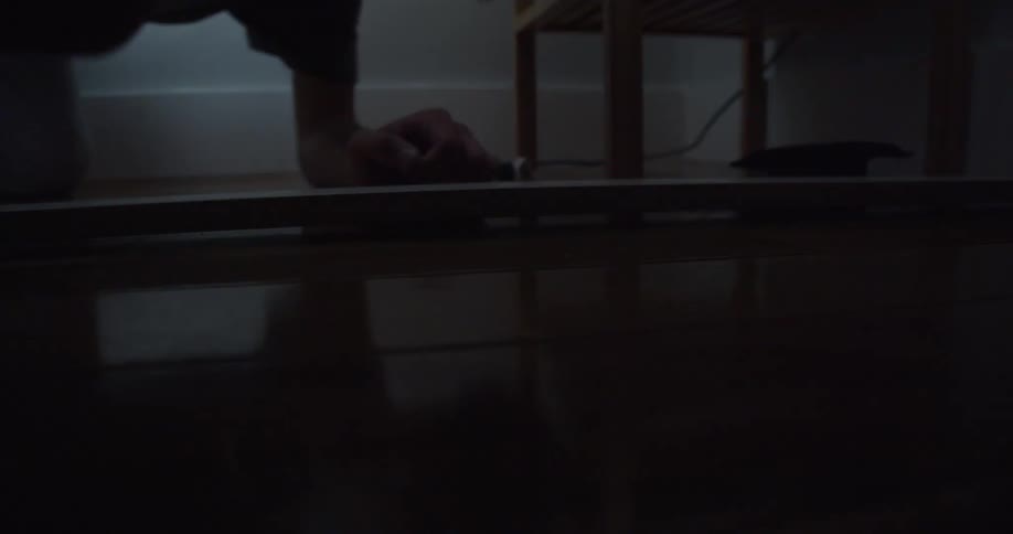 A teenage boy gets down on the floor at home and looks under some furniture