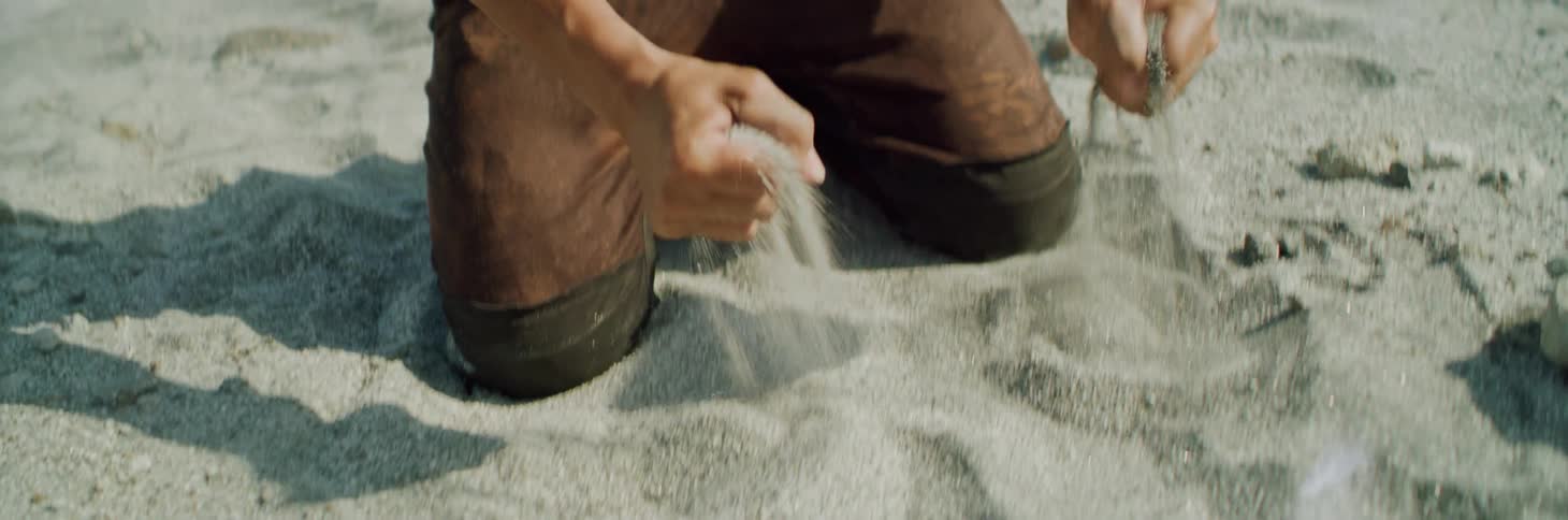 Long haired man falls to his knees and grabs sand