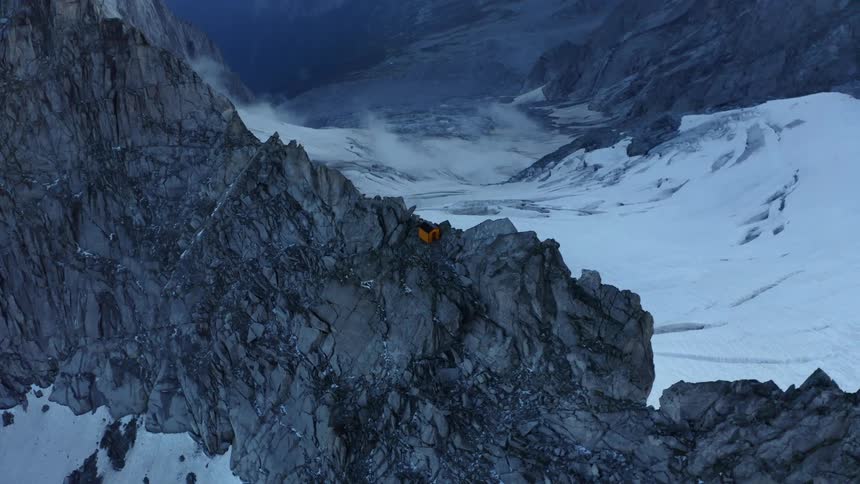 A small shelter sits on a narrow rocky mountain ridge