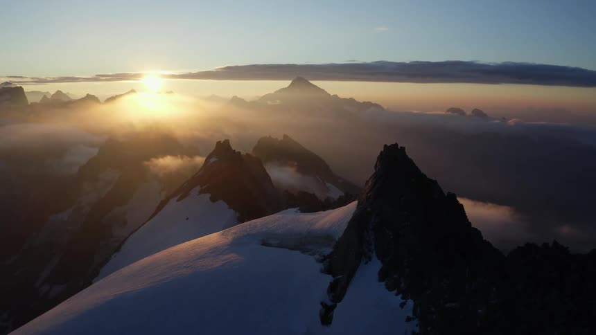 The sun glows golden on rocky mountain peaks with snow covered slopes