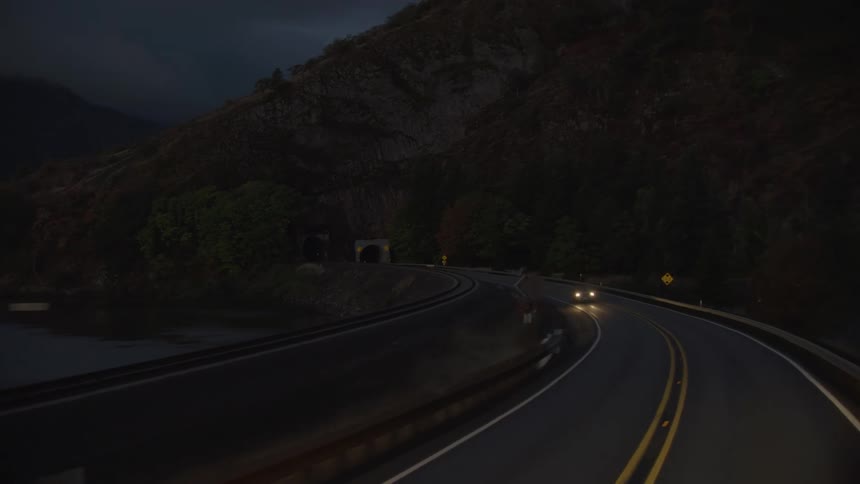 Driving on a small two lane highway before the sun rises in beautiful early morning blue light with a tunnel in the background