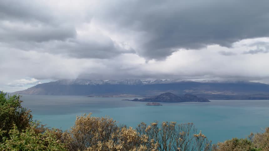 Dark storm clouds hang over a coast area of an ocean near the mountains