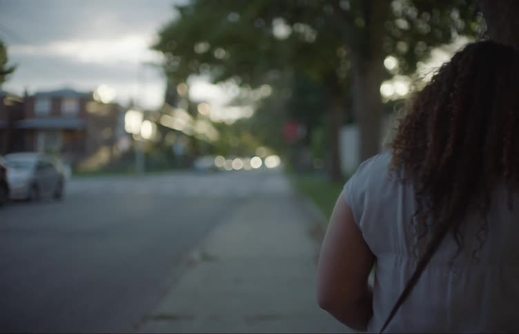 Woman with curly hair grey t shirt and mini handbags walks down the street on the sidewalk in the neighborhood