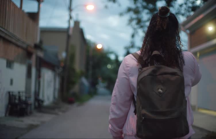 A female walks alone in a city alley with a backpack