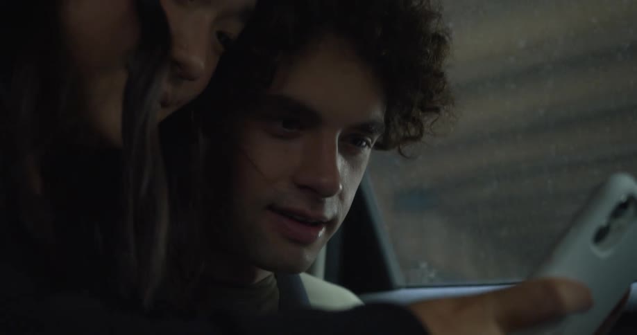 Man with curly hair and green t shirt and woman with straight hair and black sweater use smartphone in car driving on highway