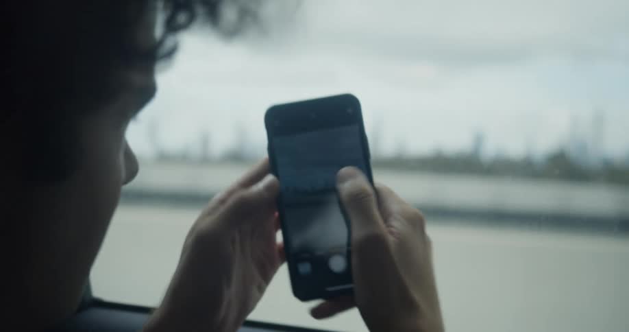 Young man takes pictures of the city skyline from a moving car driving over a bridge