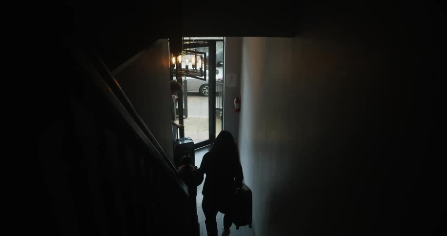 Two people carry their luggage down the stairs