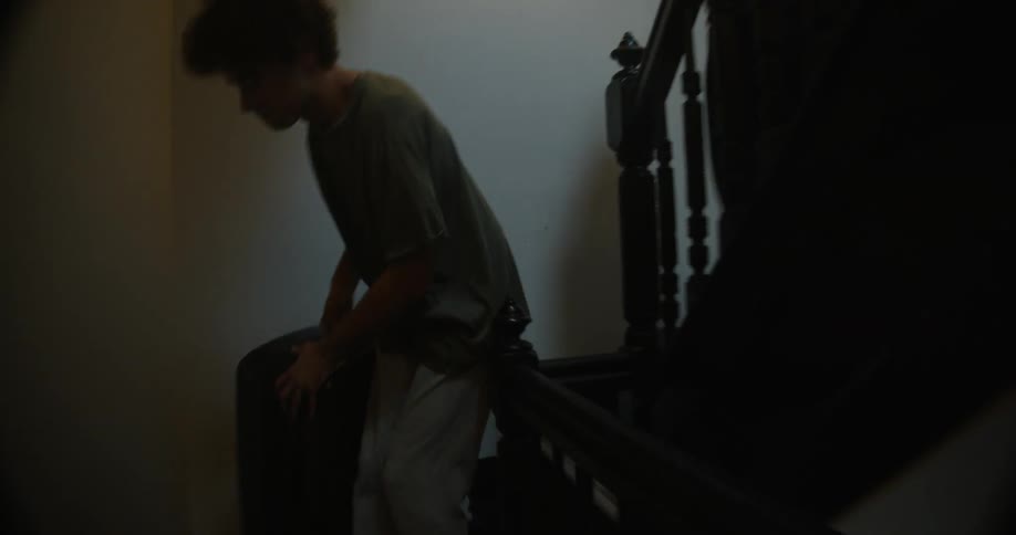 Man carries suitcase down stairs before placing it on ground and rolling it down hall