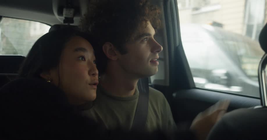 A man and woman point at things as they travel by taxi