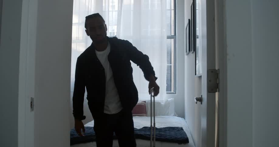 Young man picks up luggage and exits a bedroom