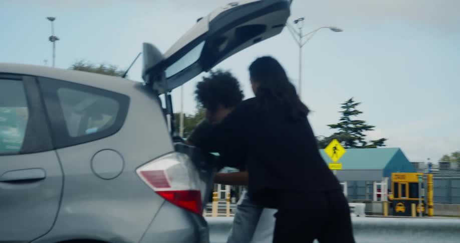 A man and woman take luggage out of the rear of a vehicle and walk away with it