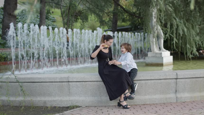 Mother and son sit on side of fountain playing with toy