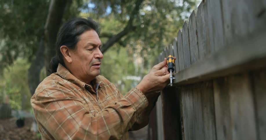 A man is repairing the fence in his yard