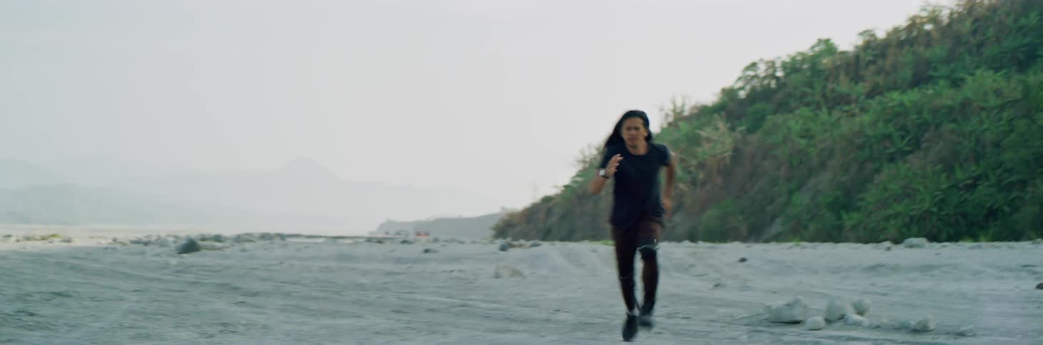 Man runs across sand away from hill with fog obscuring mountains on horizon