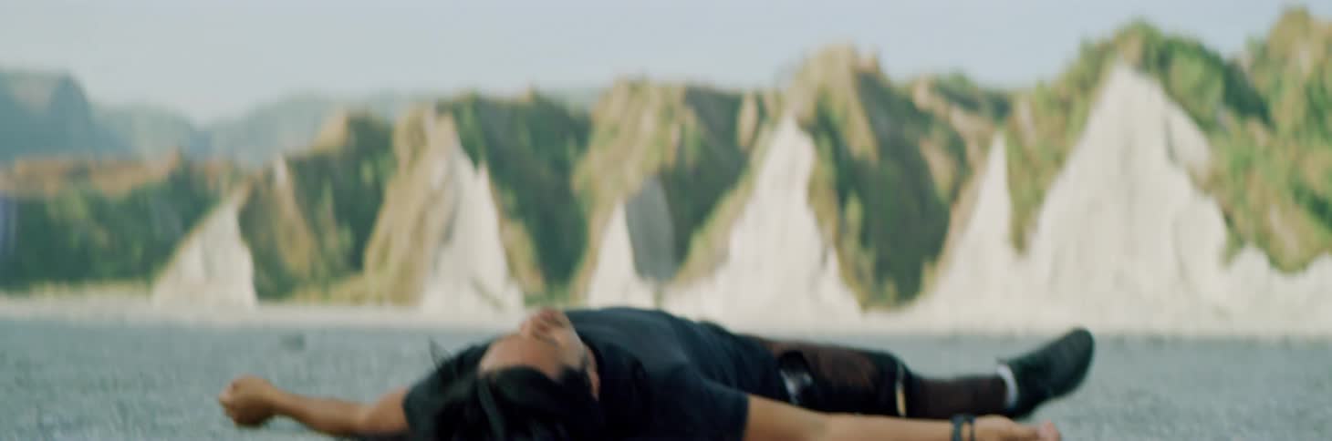 A man lies with arms outstretched on the ground near pointy brush covered dunes