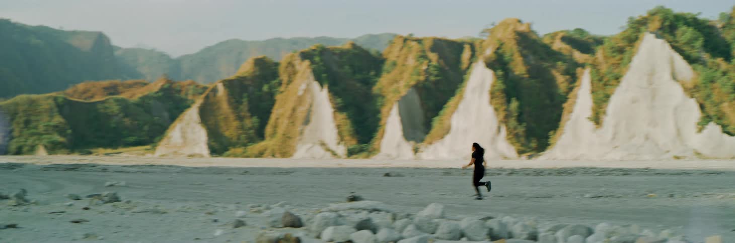 Man runs across sand passing forest covered mountains