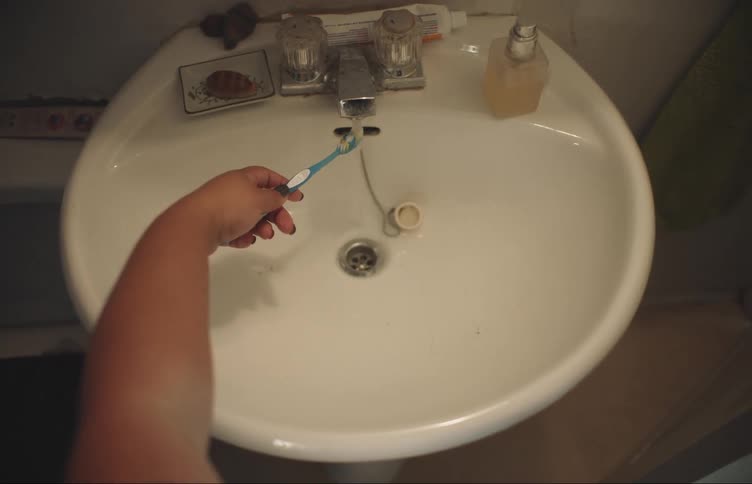 A person puts their toothbrush under the running water in a sink