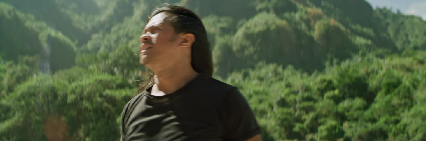 Man stretches his arms out facing upward toward the sky with misty mountains in background