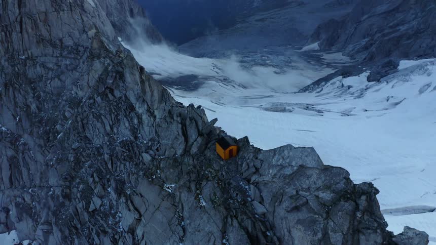 Orange building sits on ridge near snowy valley leading to water