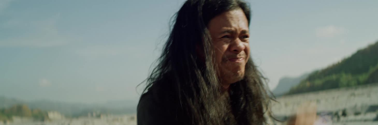 Young man with long hair shakes his fist in anger while standing outdoors