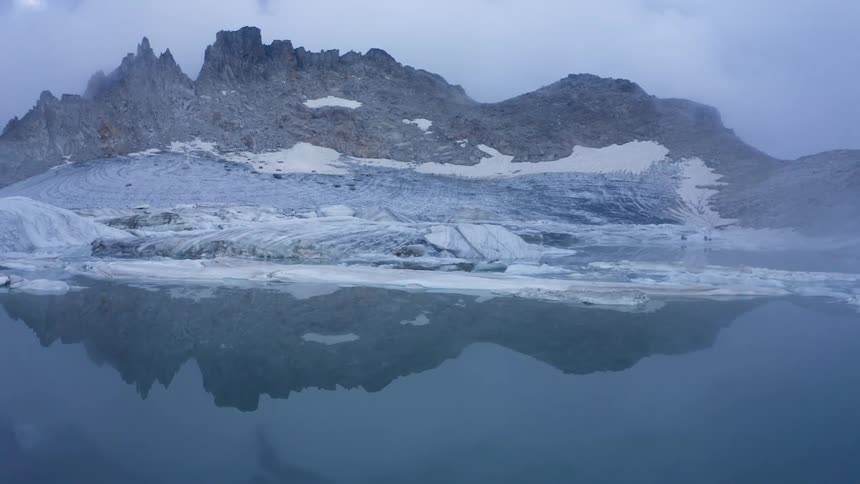 Water reflects glacier and nearby mountain on misty day