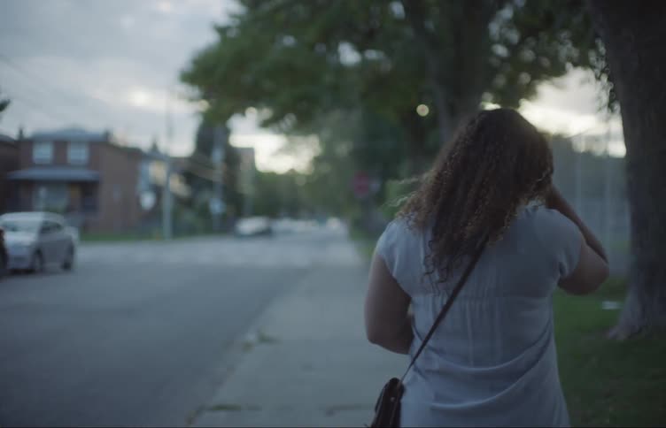 A woman walks down a sidewalk in a quiet neighborhood