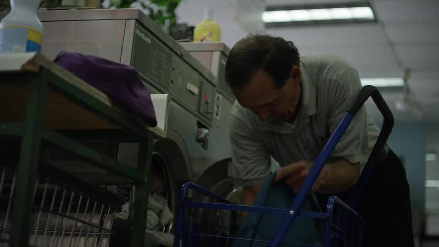 An older man places clothes into a washer in a laundromat