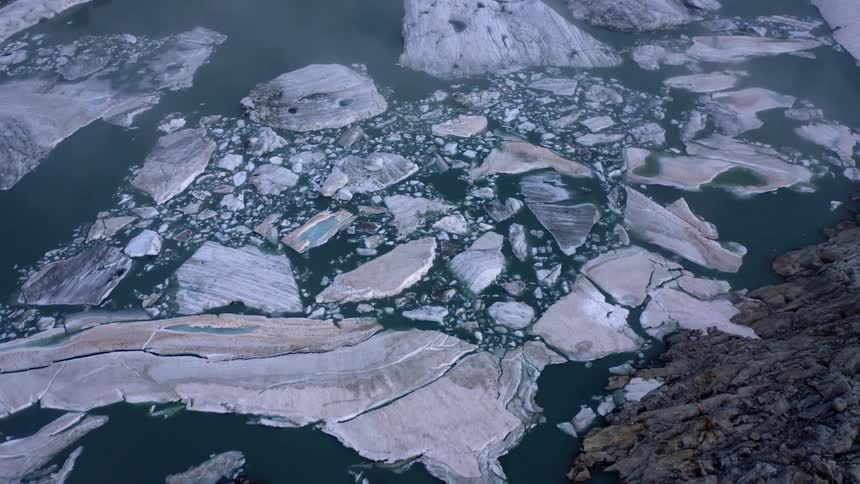 Ice sheets floating on the surface of a lake in near the coastal rocks in the mountains