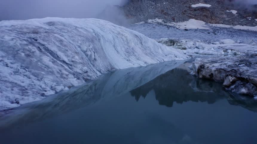 Glacier borders sky reflecting water near foggy mountain