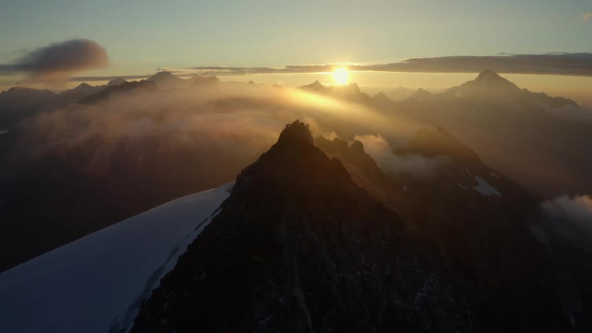 Snow covered mountains with peaks high above the clouds as the sun is setting in the distance