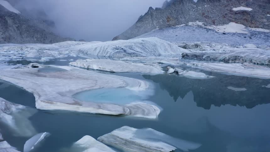 Ice floats on reflective water near glacier and mountains on foggy day