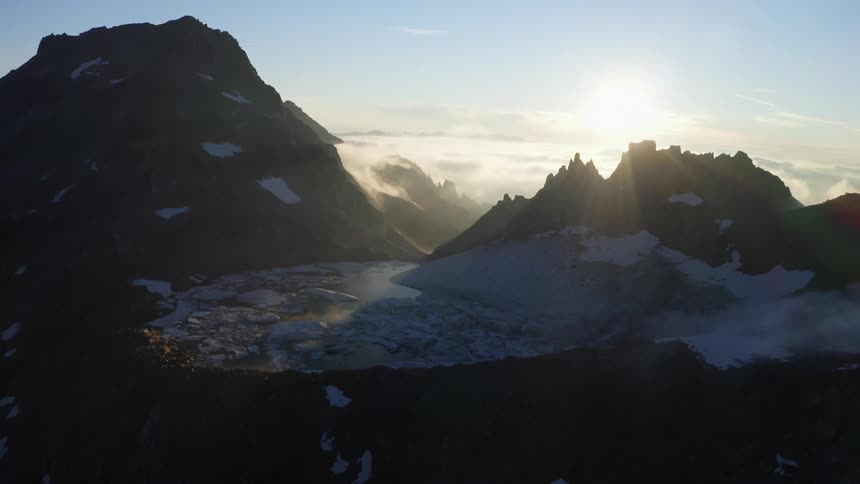 The sun is rising above the ice lake at the top of the mountain