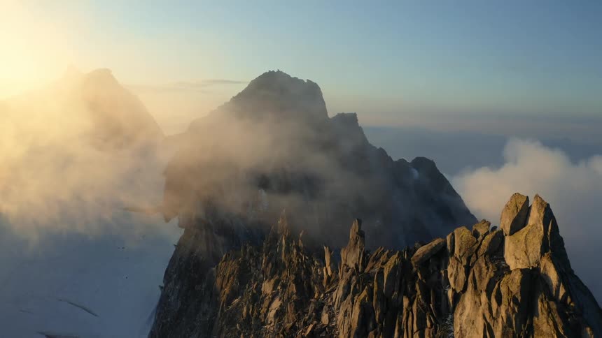 The sun shines brightly on mountain peaks high above the clouds