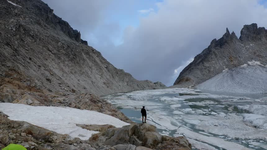 A man stands on the rocks by the ice covered lake on the mountain